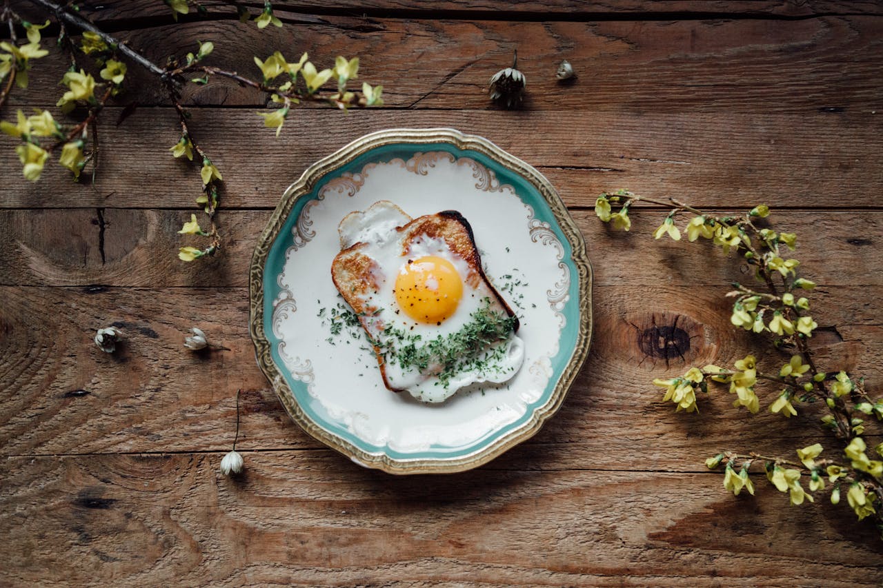 Beautifully plated fried egg on toast with herbs on a rustic wooden table, surrounded by yellow flowers.