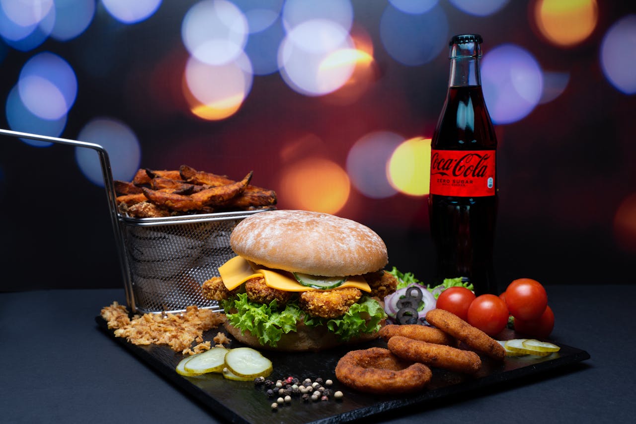 A gourmet burger meal with fries, onion rings, and soda against a vibrant bokeh background.
