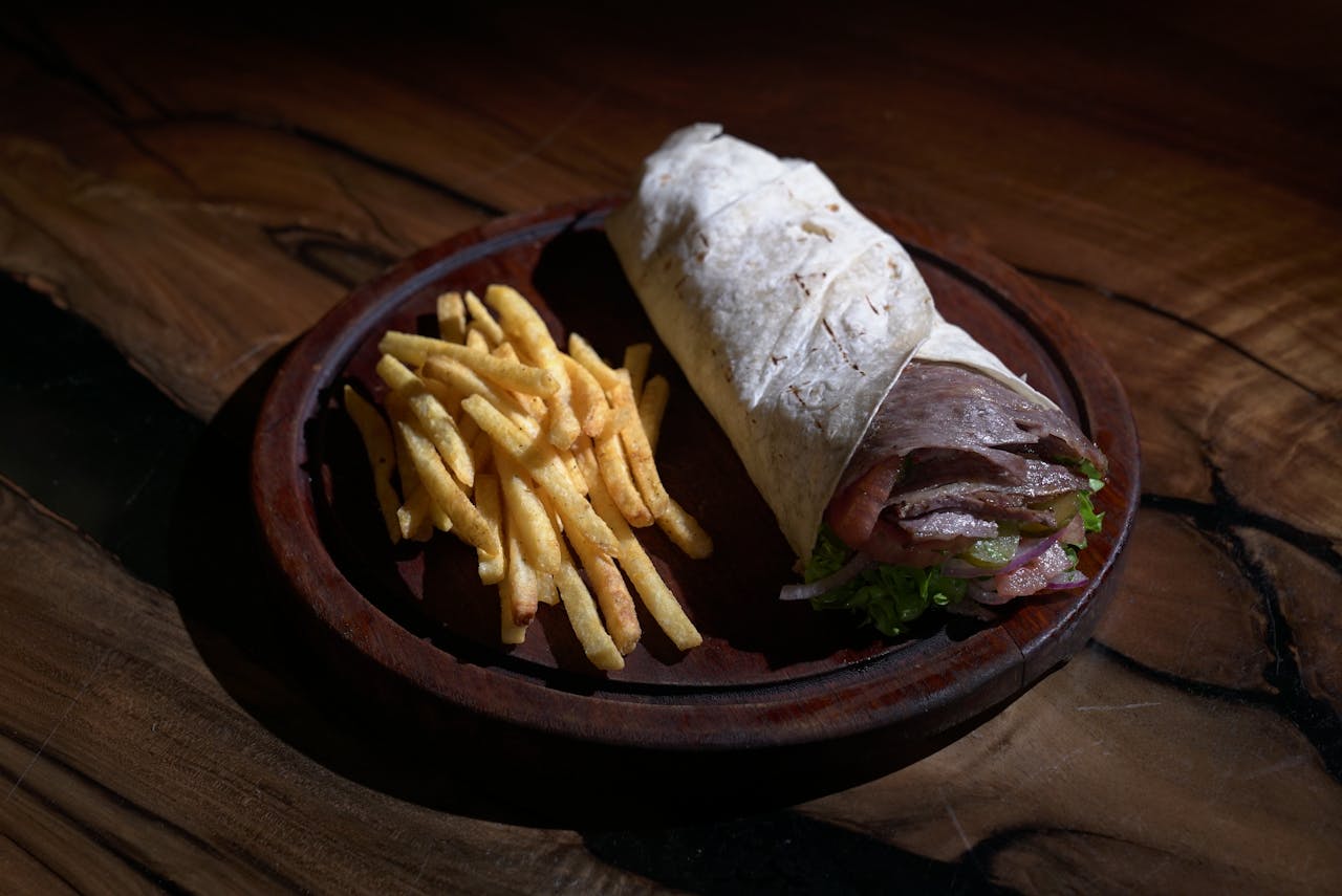 Delicious beef wrap served with crispy french fries on a rustic wooden plate.